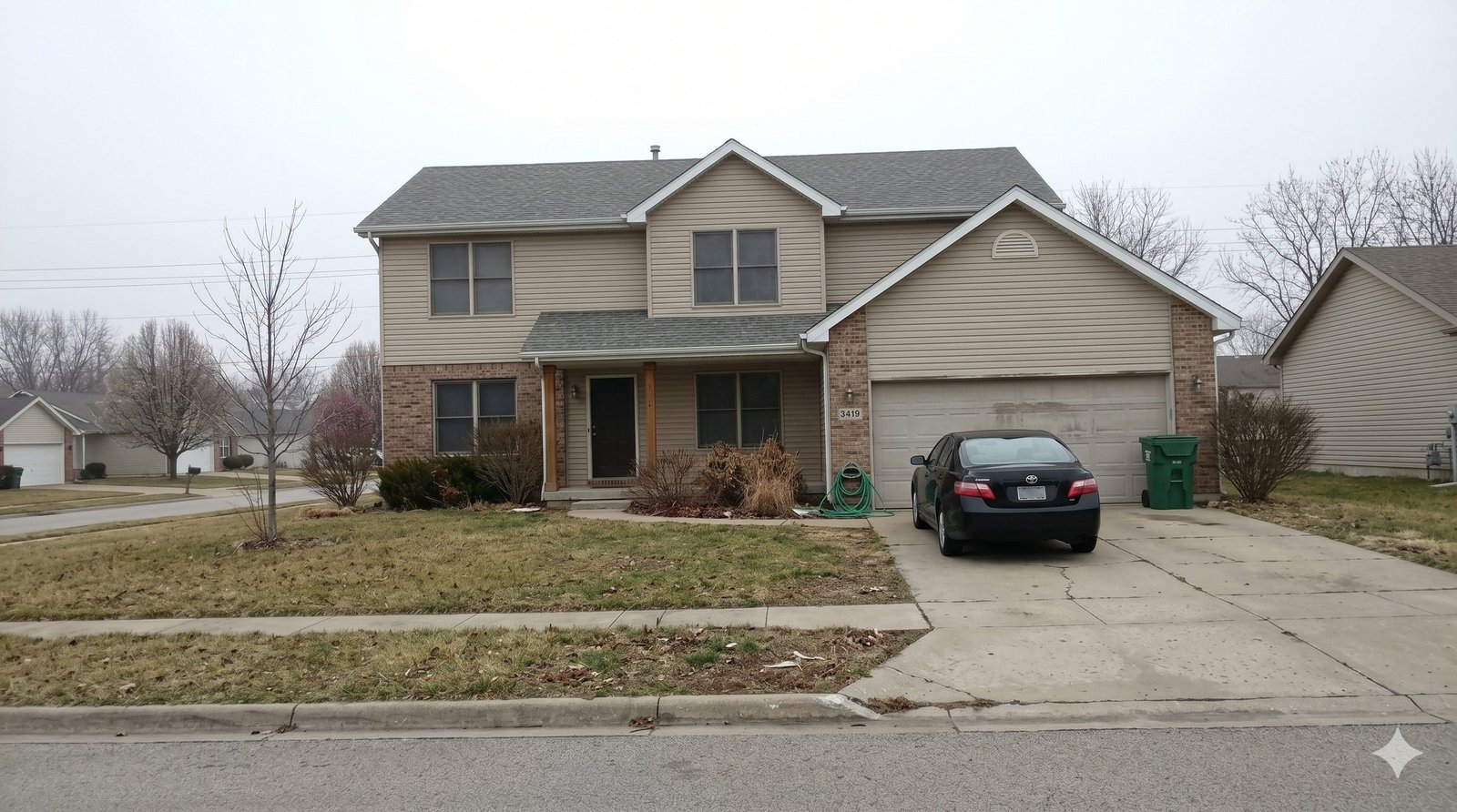 Home exterior raw camera capture: overcast gray sky, dormant brown lawn, vehicles and bins in view
